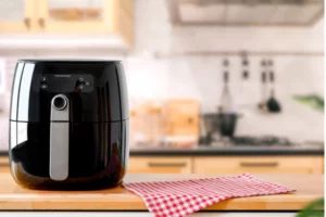 air fryer em cima de um bamcao com um fundo de cozinha e um pano vermelho ao lado